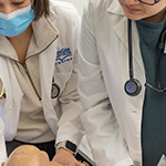 two people in labcoats standing over a mannequin baby. One person has a stethoscope around their neck.